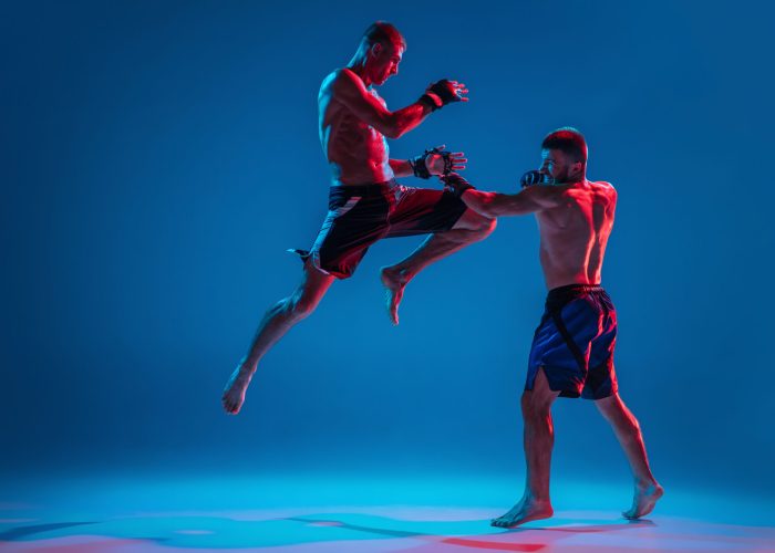 Tensioned. MMA. Two professional fighters punching or boxing isolated on blue studio background in neon. Fit muscular caucasian athletes or boxers fighting. Sport, competition and human emotions, ad.